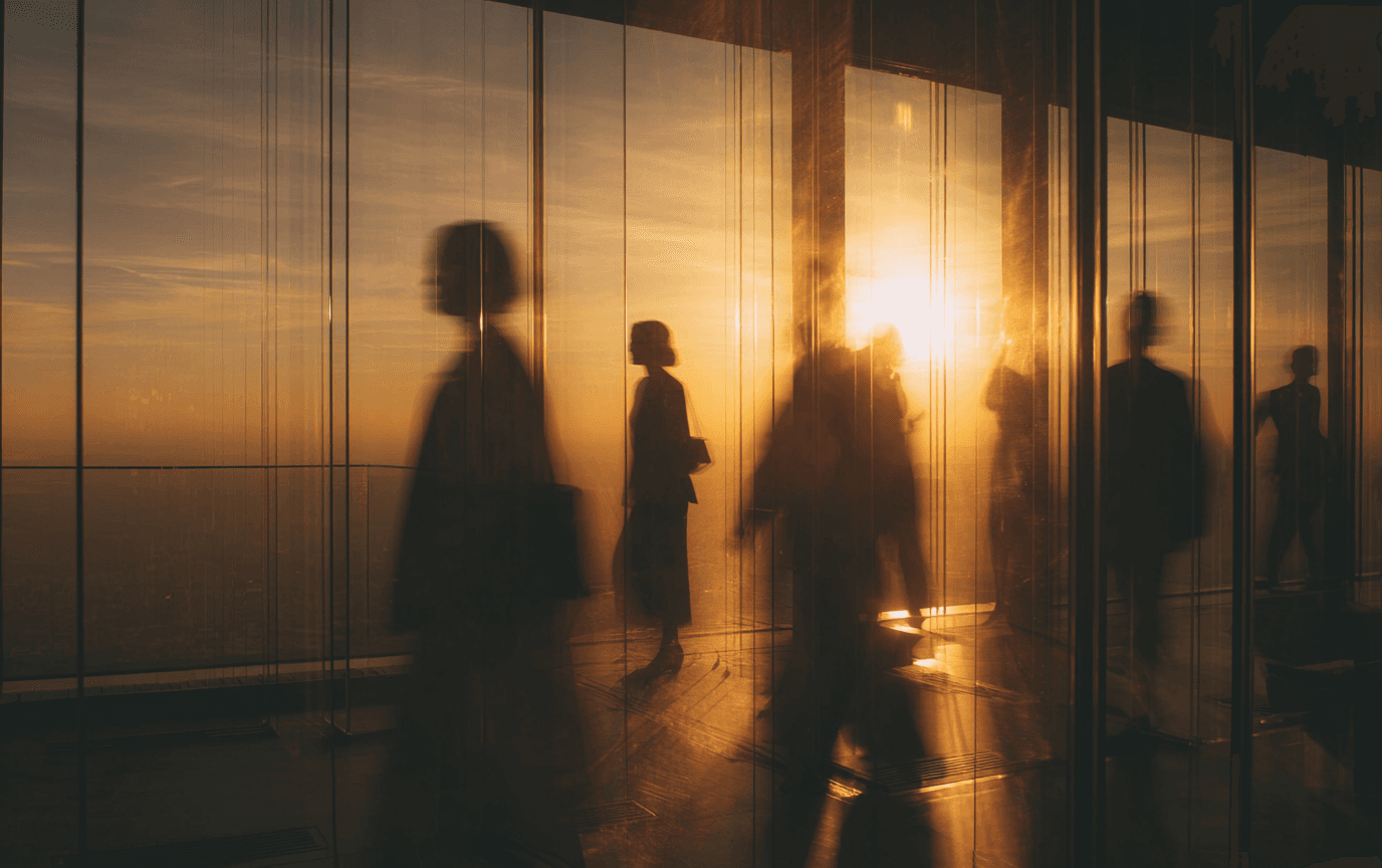 Silhouettes moving through a glass office at golden hour